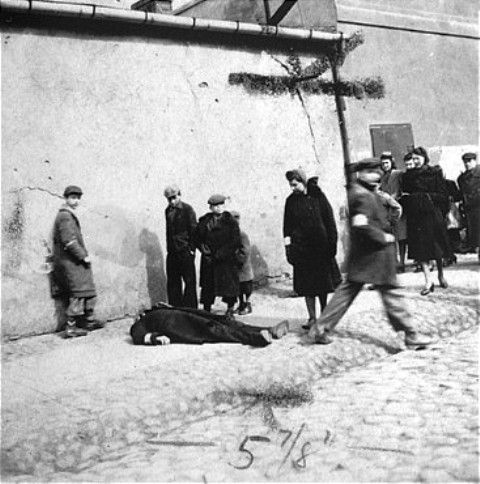Warsaw ghetto residents stare at a man who has collapsed in the street